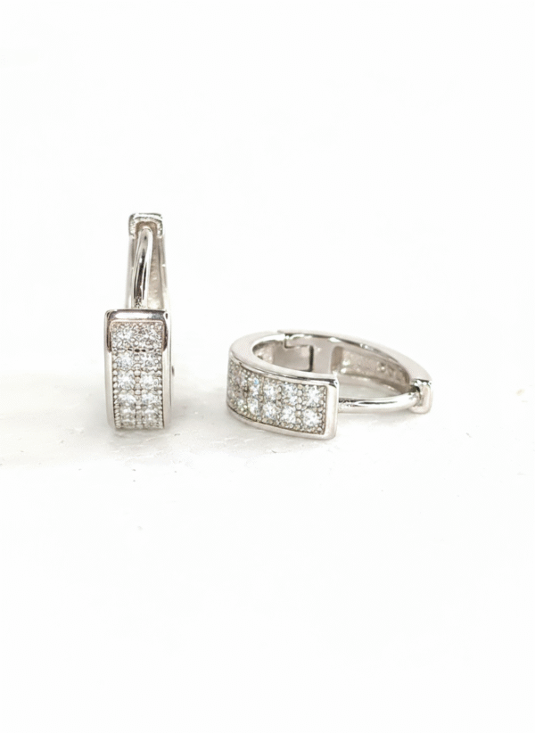 Pair of shiny silver unisex huggie hoop earrings with pave-set white cubic zirconia stones. Features a hinged snap-bar clasp and made from 925 sterling silver.
