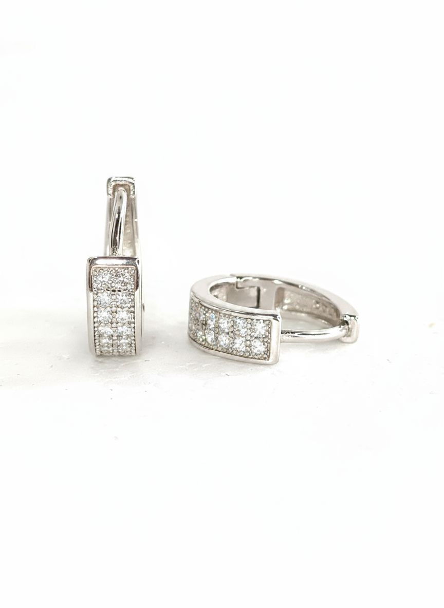 Pair of shiny silver unisex huggie hoop earrings with pave-set white cubic zirconia stones. Features a hinged snap-bar clasp and made from 925 sterling silver.